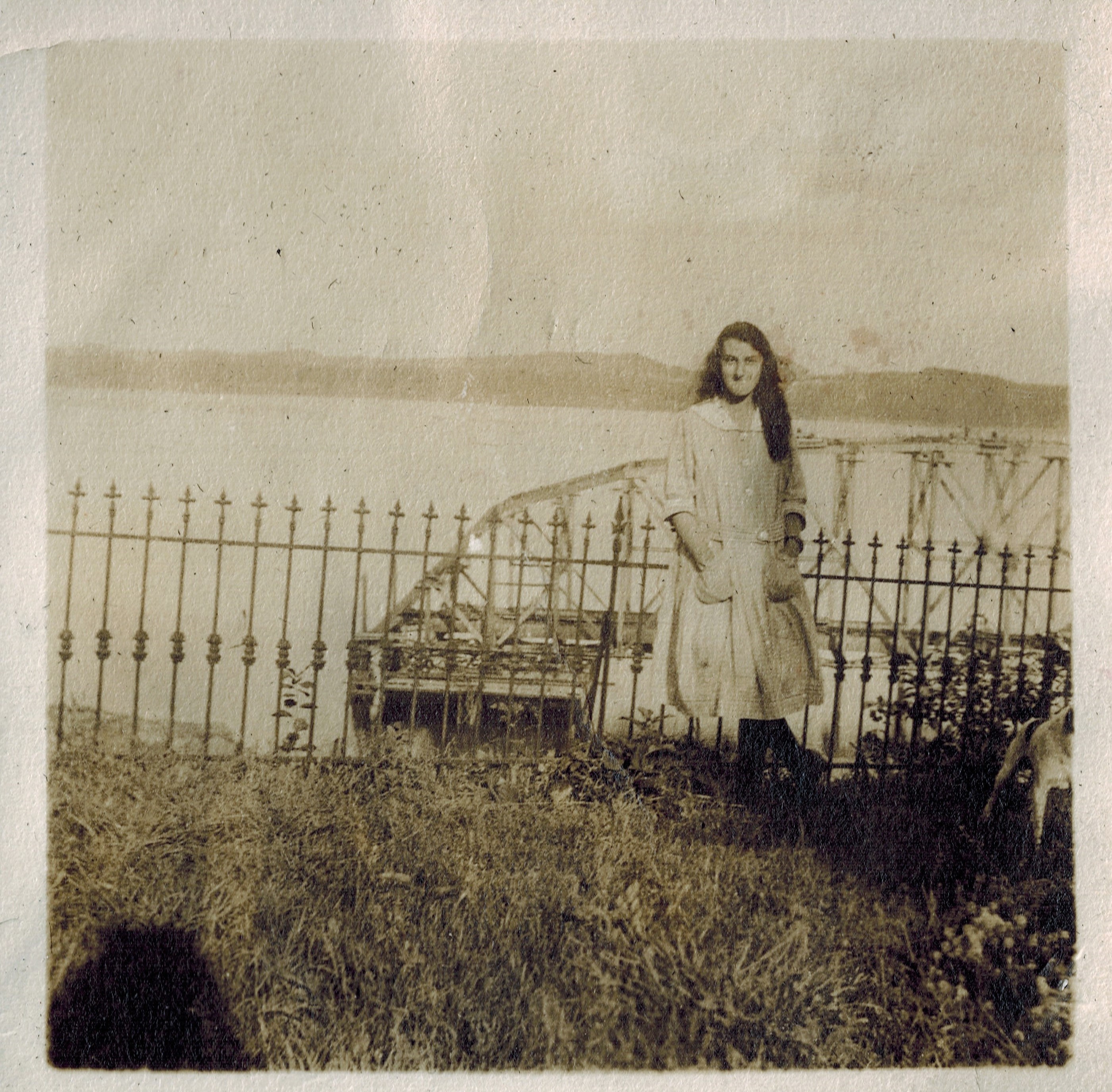 photo sépia d'une jeune fille vêtue d'une robe blanche devant un pont