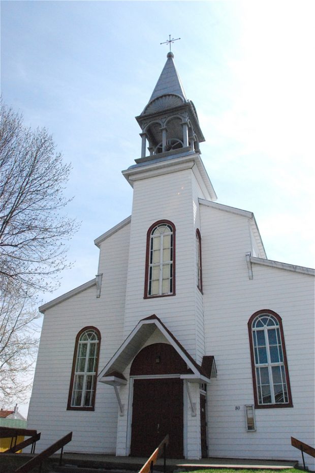 Photographie couleur, plan rapproché, façade d’une église en bois peint en blanc comprenant le clocher et le portique.