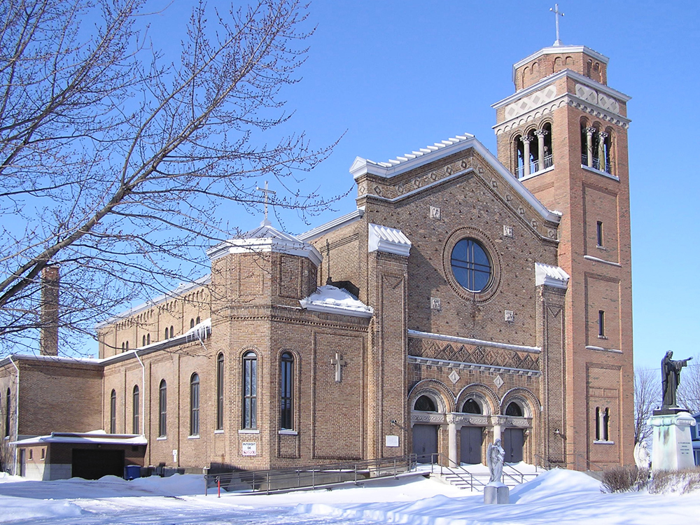 Photographie couleur prise en hiver, plan éloigné, grande église en briques avec un imposant clocher à la droite du bâtiment.