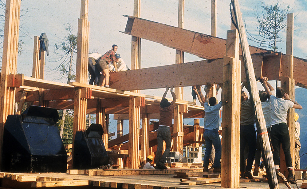 Plusieurs membres s’adonnent au travail de construction, en soulevant une solive de plancher tout en essayant de la placer convenablement.