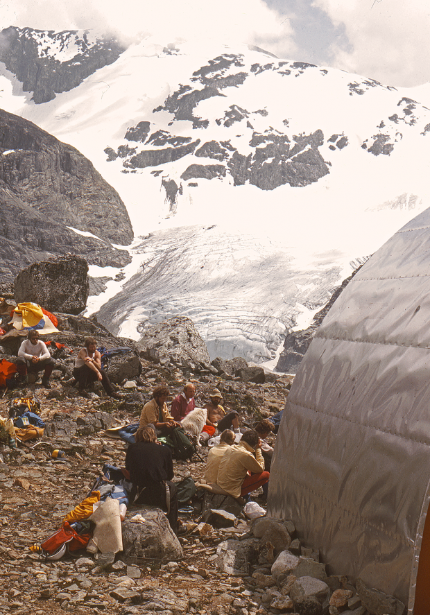 Le côté du refuge du lac Wedgemount se trouve au premier plan et un groupe de personnes sont assises sur les rochers à l’extérieur du refuge. Le mont Wedge et le glacier se trouvent en arrière-plan.