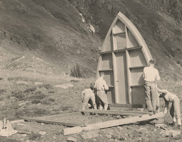 Deux hommes tiennent un côté du mur d’extrémité avant voûté tandis que trois autres fixent l’autre côté à la fondation.