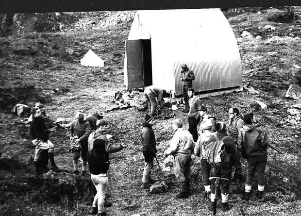 Un groupe d’étudiants se tiennent devant le refuge Batzer ainsi qu’à sa droite, dans la prairie alpine verdoyante.