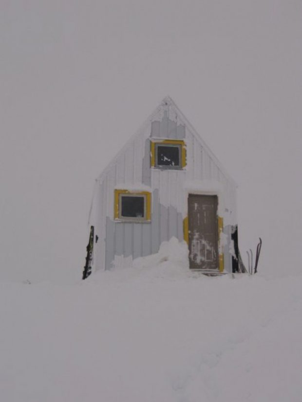 Le ciel gris est menaçant derrière le refuge. Les fenêtres aux encadrements jaunes et la porte principale ont été balayées par la neige.