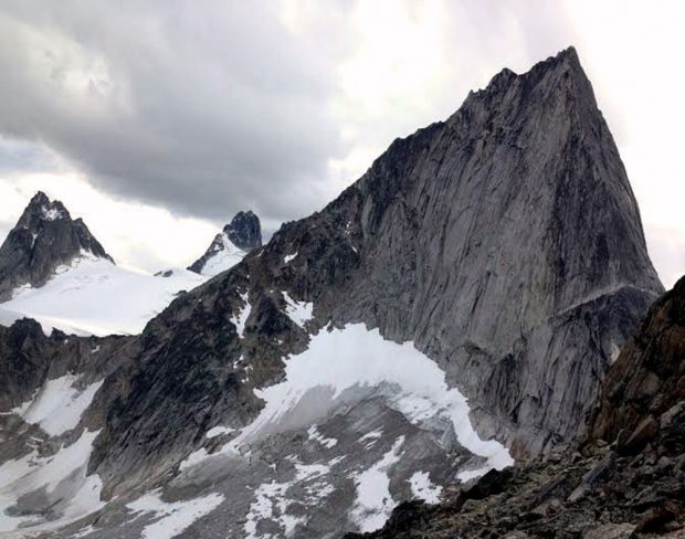 La cime de la flèche étroite et grise avec son pic aux contours irréguliers se dresse au-dessus d’une pente recouverte de neige sur un sol en gravier. Deux autres pics de la flèche grise s’élèvent d’un glacier situé à proximité de la crête de la flèche au premier plan.