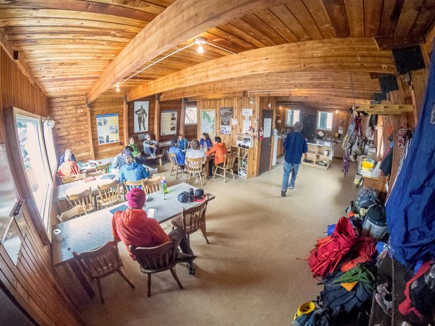 Un groupe de personnes sont assises aux tables de la pièce principale ouverte et l’espace cuisine situé au coin arrière droit est plein de monde.