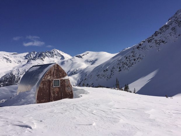 Le mur d’extrémité du refuge montre des signes d’érosion importante et la neige ainsi que les environs sont baignés de soleil.