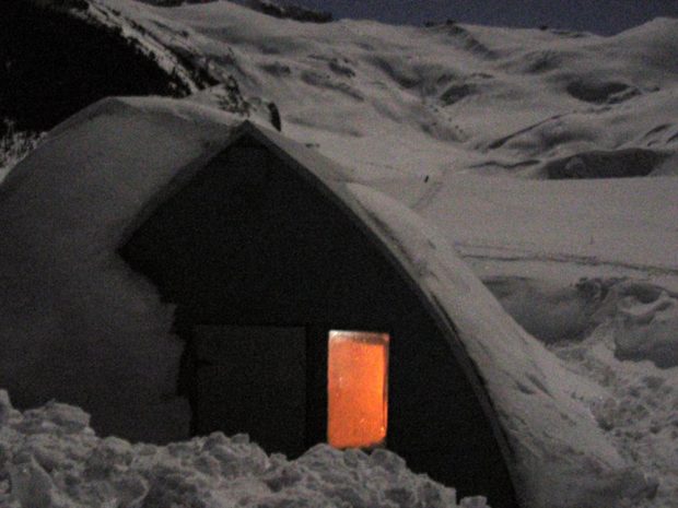 Un refuge partiellement enfoui sous la neige avec de la lumière luisante de l’intérieur à travers la fenêtre béante.