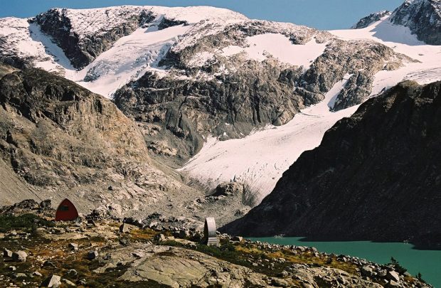 Le mont Wedge et son glacier se dressent au-dessus du refuge voûté de style gothique bâti au milieu d’un pré rocheux se trouvant en contrebas. Les toilettes extérieures du refuge sont munies d’un revêtement en aluminium et sont situées à une certaine distance de celui-ci et près du lac Wedgemount.