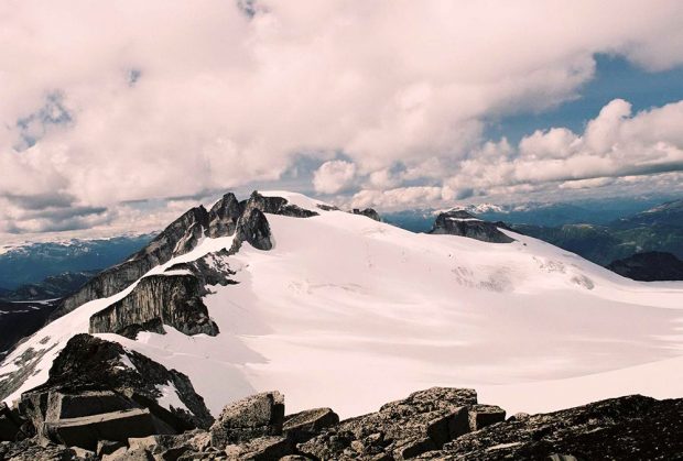 Deux des trois sommets du mont sont à découvert tandis que le troisième est masqué par la neige. Des nuages floconneux blancs flottent au-dessus des trois sommets.