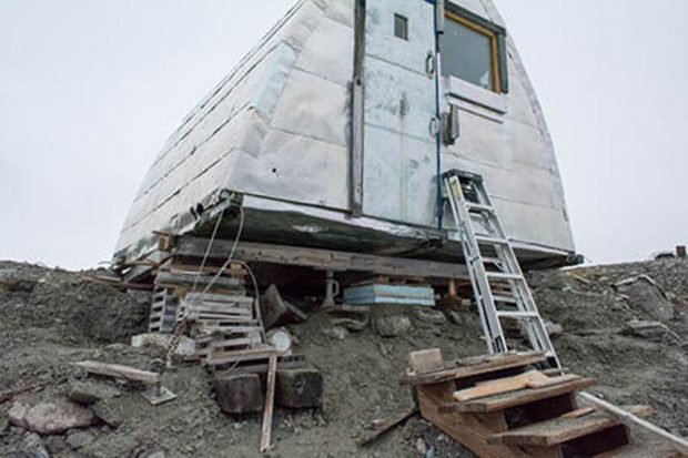 Refuge voûté de style gothique revêtu d’aluminium soutenu par des blocs de bois en raison de l’érosion du sol. Les escaliers en bois visibles en premier plan ne sont plus fixés au refuge.