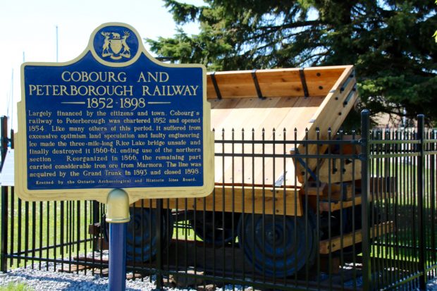plaque commémorative bleue de la province de l’Ontario relatant l’histoire de la Cobourg and Peterborough Railway. La plaque est installée devant une réplique grandeur nature d’un wagon de minerai près de l’endroit où l’original fut construit en 1867.