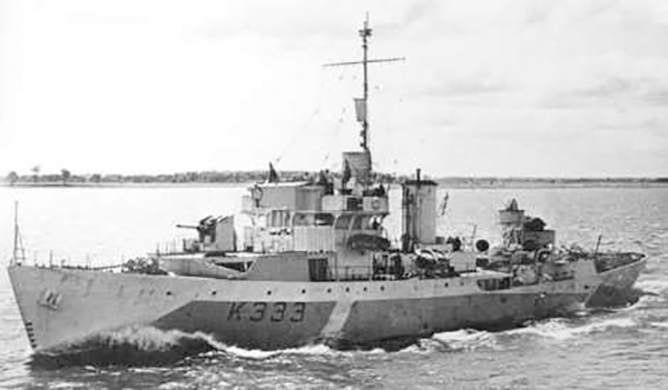 Une photo en noir et blanc d’un navire de guerre de type corvette, avec l’inscription K333, naviguant au large en direction de la rive.