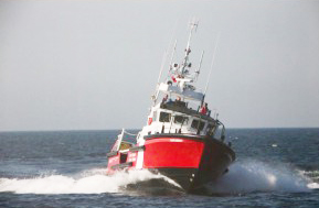 Photo en couleurs d’un vaisseau rouge et blanc en eau libre qui se dirige vers l’appareil-photo.