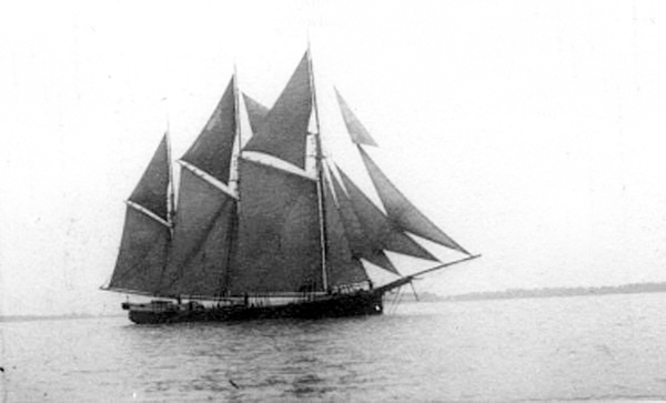Une photo en noir et blanc d’un navire à voiles avec trois mâts naviguant au large avec toutes les voiles déployées.