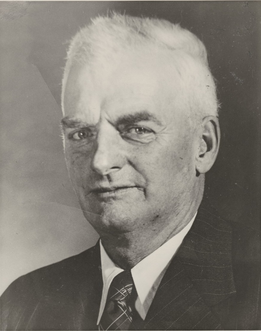 Photo de M. Frank Bickle face à l’objectif avec des cheveux blancs et courts, portant une chemise blanche, une veste et une cravate