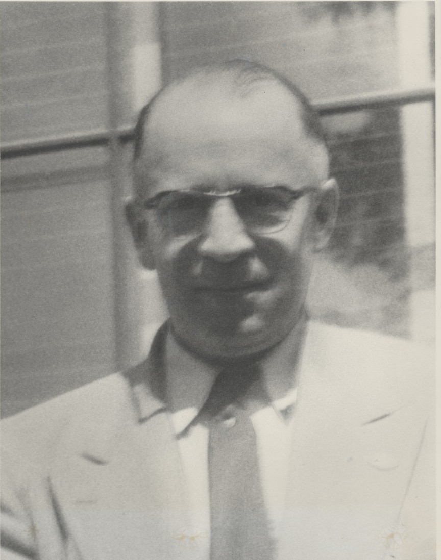 Harry F. Bickford regarde l’objectif. Il porte des lunettes, une veste, une chemise et une cravate. Il semble que la photo ait été prise dehors où Harry pourrait être debout à l’extérieur d'un bâtiment.