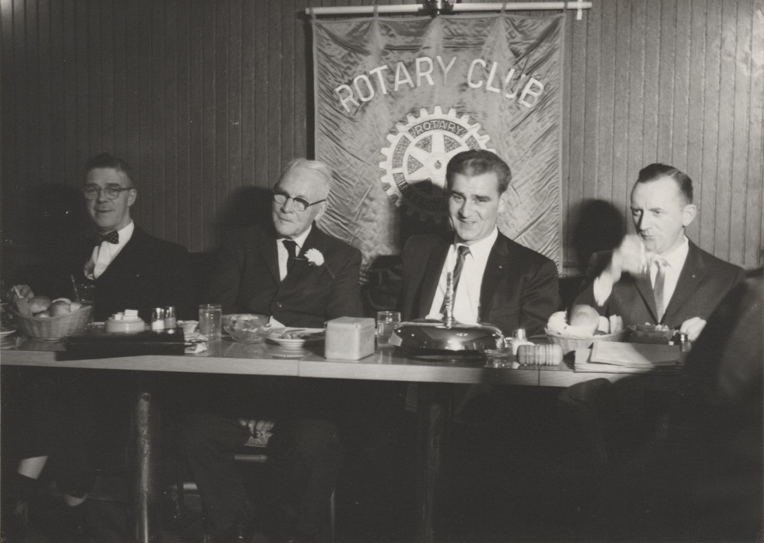 Quatre hommes bien habillés assis à une table face à l’objectif