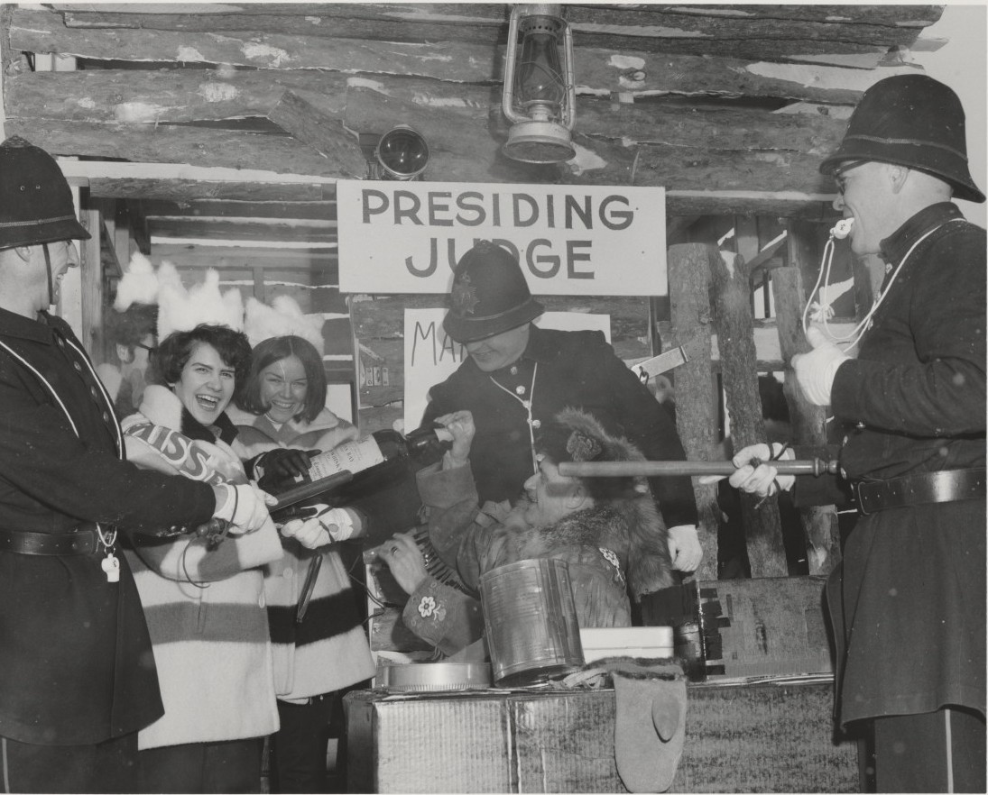 Participantes au concours de la reine des fourrures et Keystone Cops riant dans une cabane en rondins