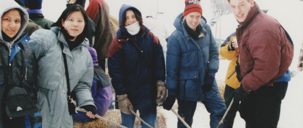 Plusieurs jeunes habillés en vêtements d'hiver qui font griller du pain bannock sur un feu. L'activité faisait partie du festival des trappeurs de 1999.