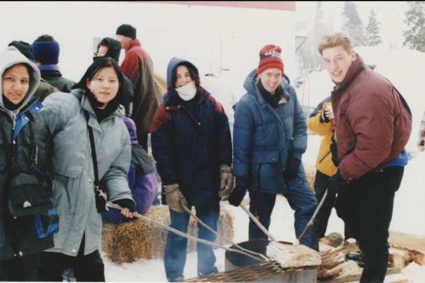 Plusieurs jeunes habillés en vêtements d'hiver qui font griller du pain bannock sur un feu. L'activité faisait partie du festival des trappeurs de 1999.