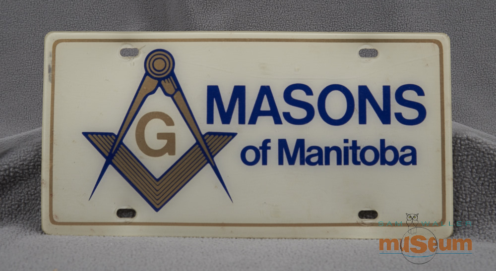 Plaque d'immatriculation blanche avec des caractères bleus pour les maçons du Manitoba et un symbole doré bordé de bleu.
