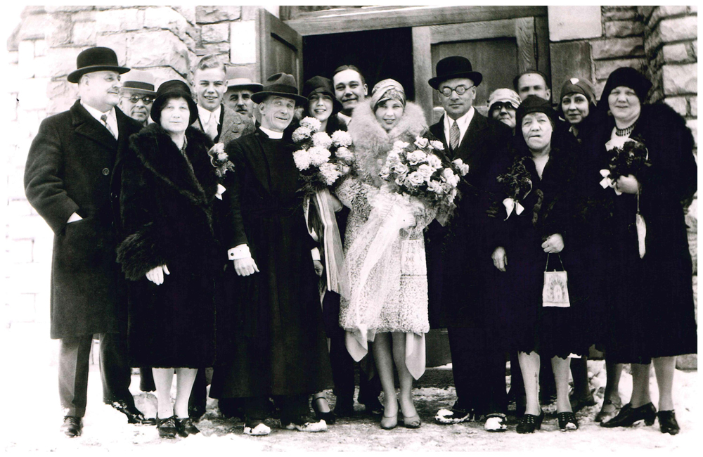 Photo de groupe du mariage de Clarence Lougheed devant une porte d’église à Banff, Isabella dans la première rangée, à côté de Clarence