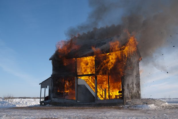 Plan fixe d’une maison coupée en deux de façon transversale et qui est en feu. 
