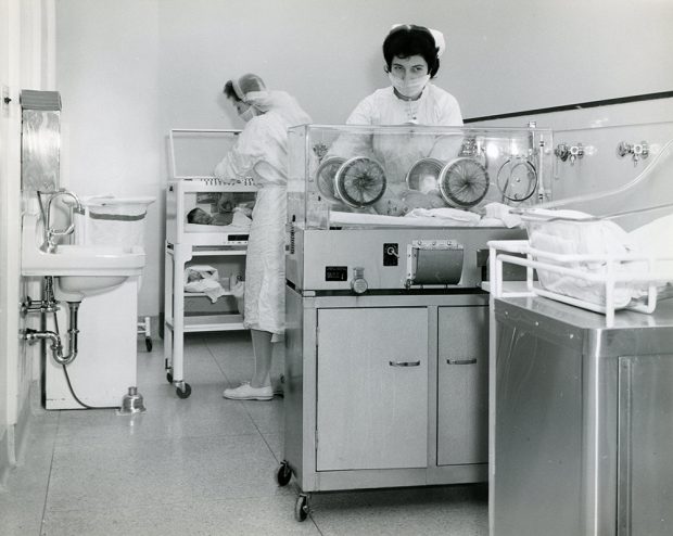 Deux infirmières avec des bébés dans des incubateurs dans une photo en noir et blanc.