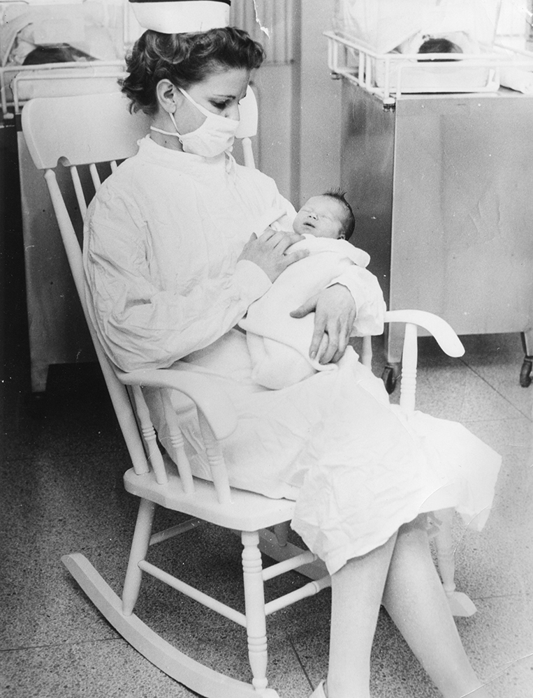Une infirmière tient un bébé dans une chaise berçante dans un hôpital dans une photo en noir et blanc.