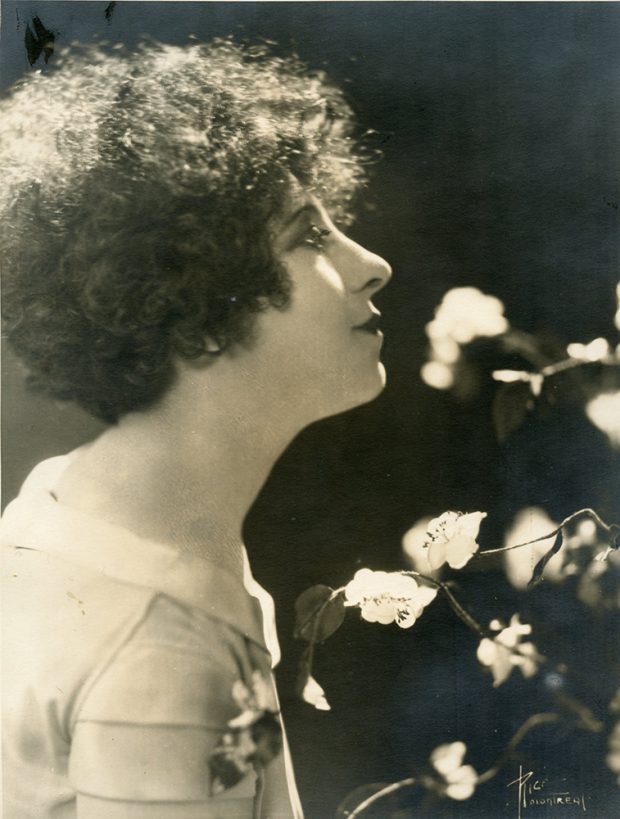 Portrait en noir et blanc de Jeanne Mignolet de profil parmi des fleurs.
