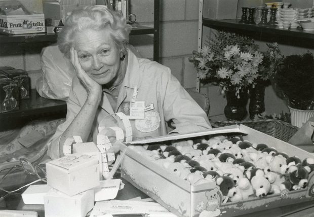 Grace Tatum assise à une table dans une photo en noir et blanc, entourée de billets de tirage et d’une boîte de nounours.