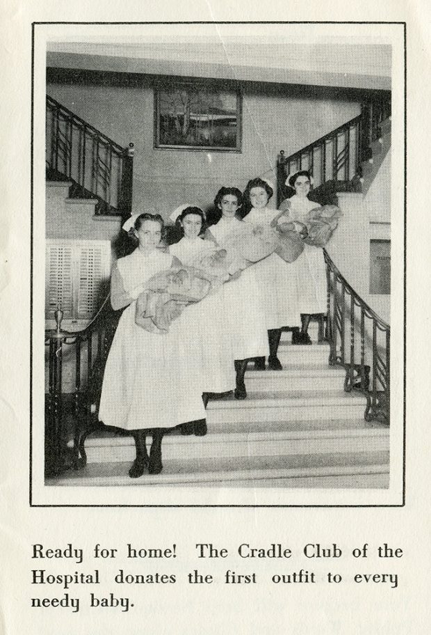Cinq jeunes infirmières posent sur un escalier tenant fièrement des bébés portant des chapeaux et enveloppés de couvertures dans une photo en noir et blanc.