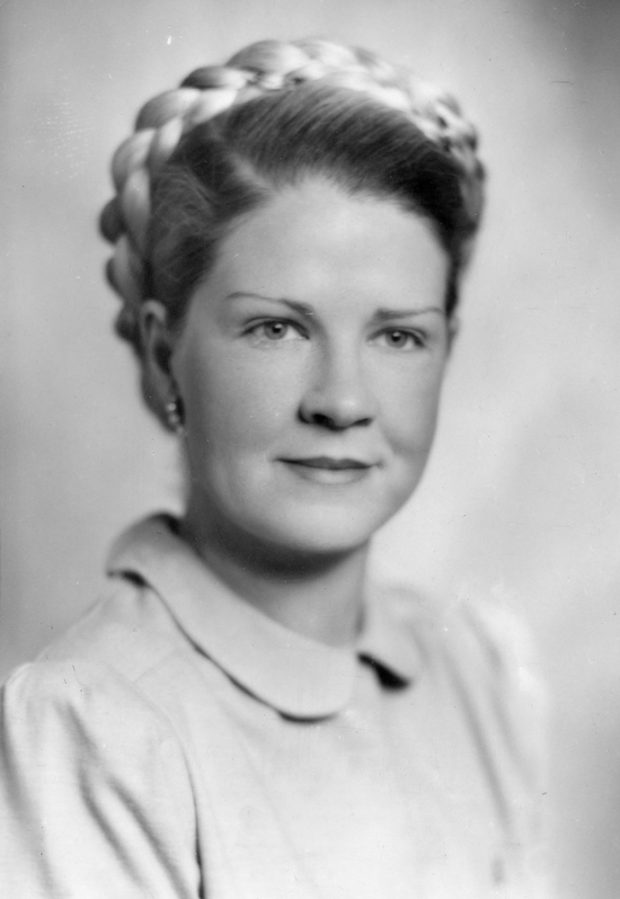 Portrait noir et blanc d’une femme souriant délicatement avec chignon tressé. 