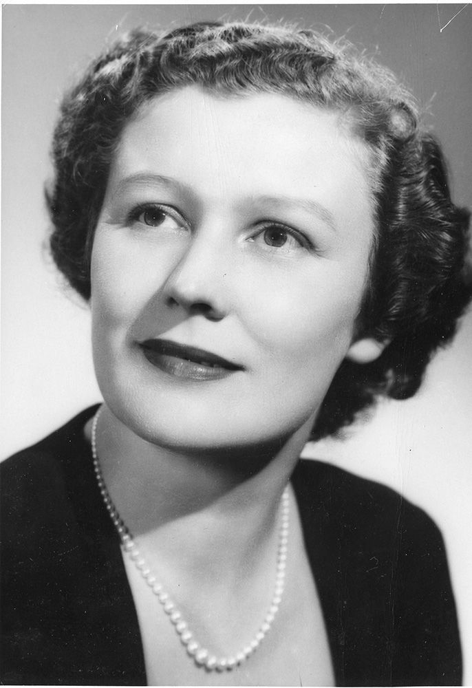 Portrait noir et blanc d’une femme souriant délicatement et portant des perles.