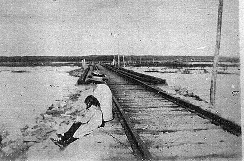 Deux personnes assises sur le chemin de fer qui traverse le marais salé