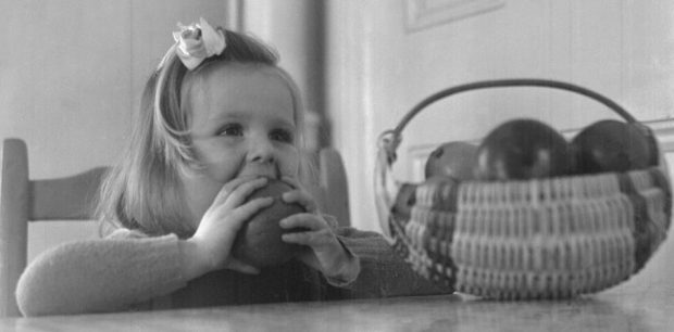 Fillette à une table croque une pomme, v.1945