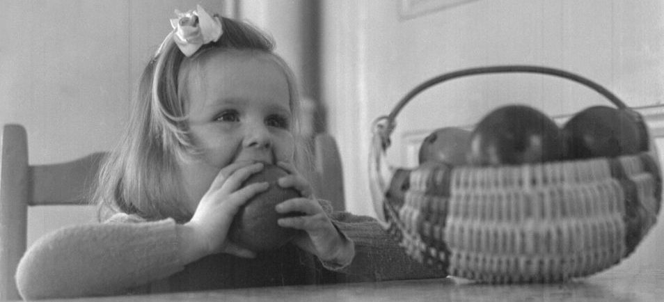 Fillette à une table croque une pomme, v.1945