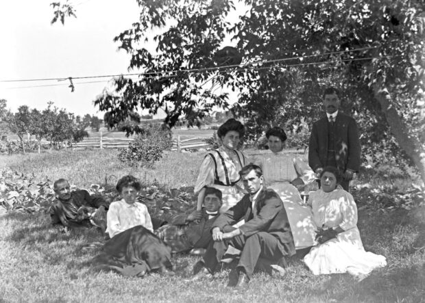 Photo ancienne d'un champ bordé de pommiers et huit personnes assises au sol