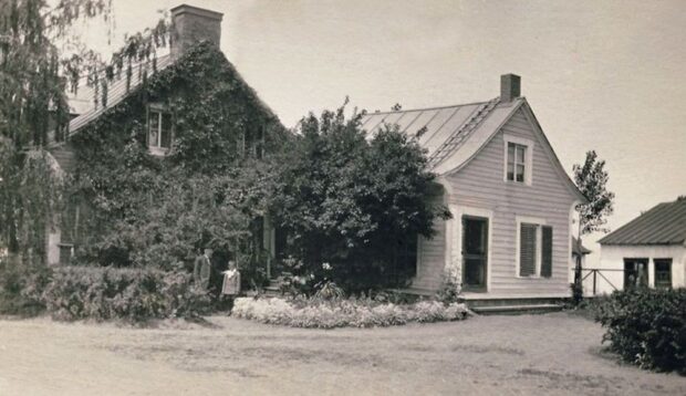 Un adulte et un enfant devant une maison recouverte de vigne près d'un annexe et d'une remise
