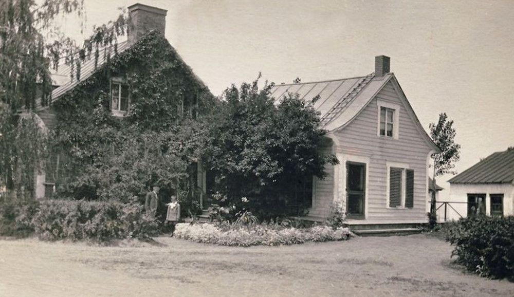 Un adulte et un enfant devant une maison recouverte de vigne près d'un annexe et d'une remise