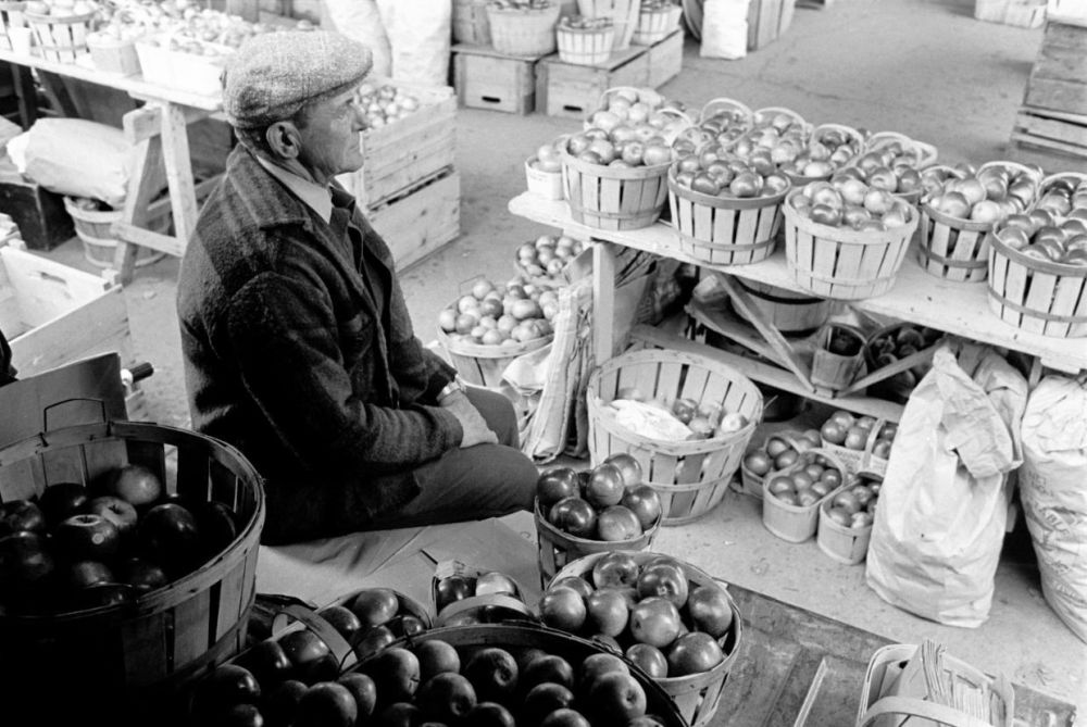 Un homme assis à son kiosque de fruits et légumes dans un marché public