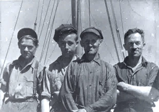 Photo en noir et blanc sur laquelle posent quatre hommes en habits de travail. Sur la gauche, deux adolescents, au centre, un homme plus âgé et à droite, un homme dans la fleur de l'âge. Derrière eux se dressent un mât et des cordages.