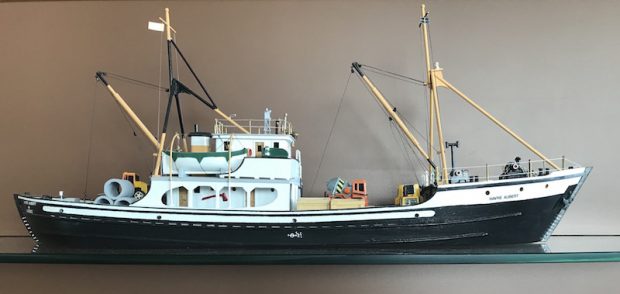 Maquette de la goélette Havre-Aubert. Le petit bateau est en bois. Sa portion inférieure est noire et la portion supérieure est blanche. Des petites chaloupes de sauvetage et du matériel de construction miniature garnissent le bateau. À la proue, on peut lire le nom de la goélette.