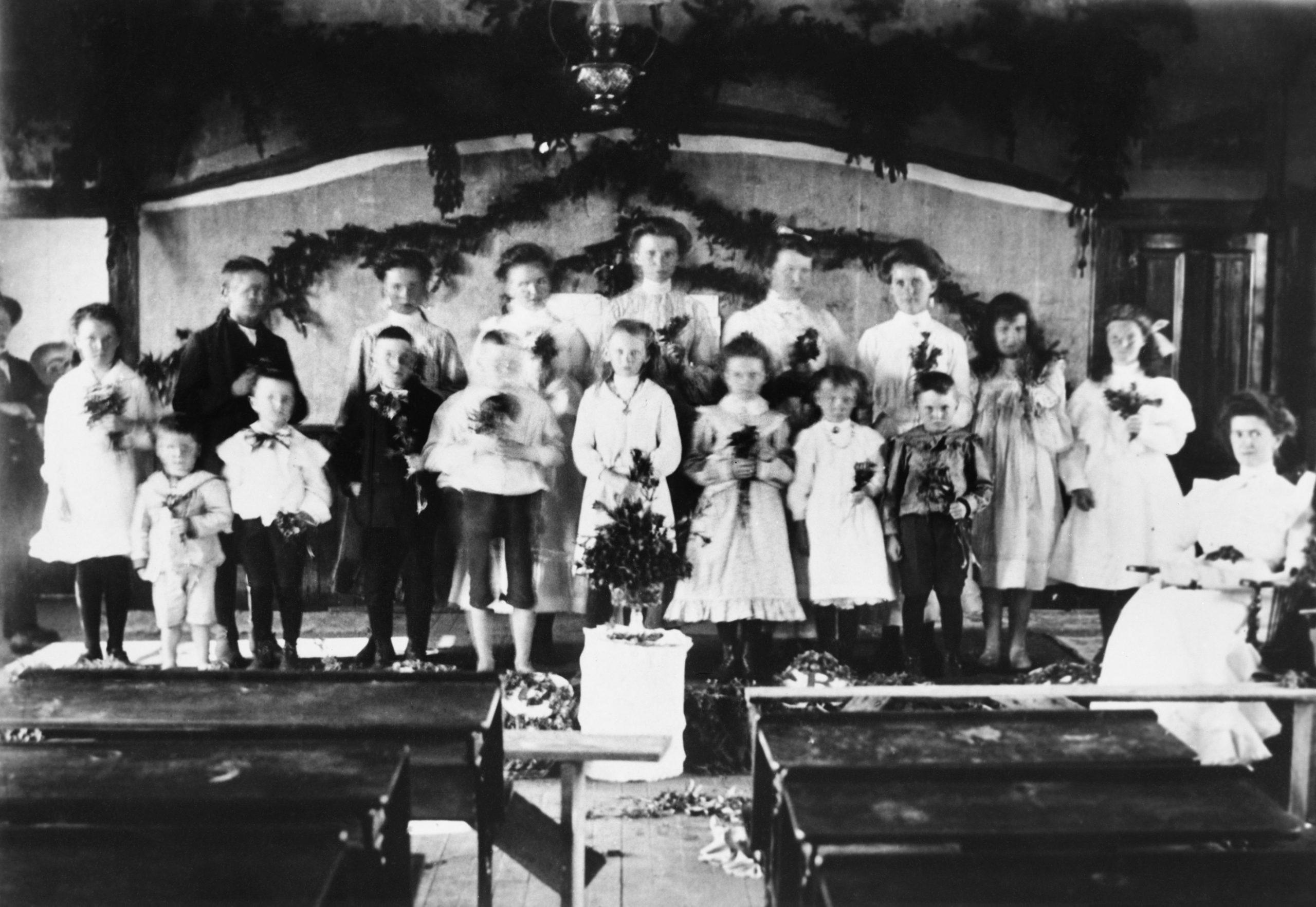 Spectacle de Noël avec des enfants sur la scène de l’école, tenant des guirlandes et un petit arbre en avant.