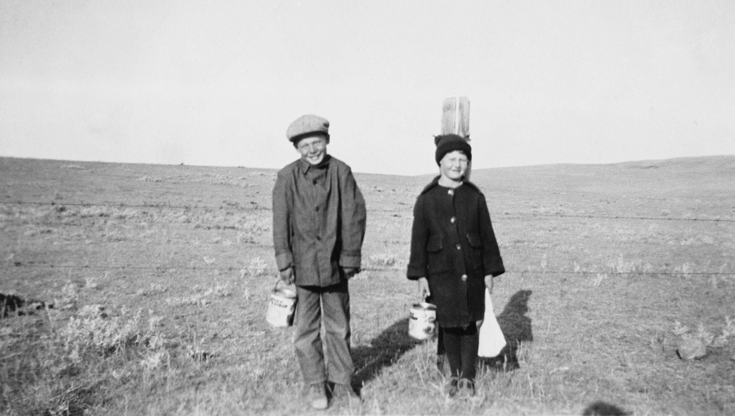Deux écoliers devant une clôture dans un champ, boîte à lunch à sirop en main.