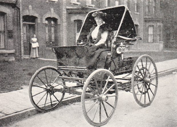 Photo noir et blanc d'une femme bien habillée assise dans une voiture électrique à toit ouvert ressemblant à une calèche.