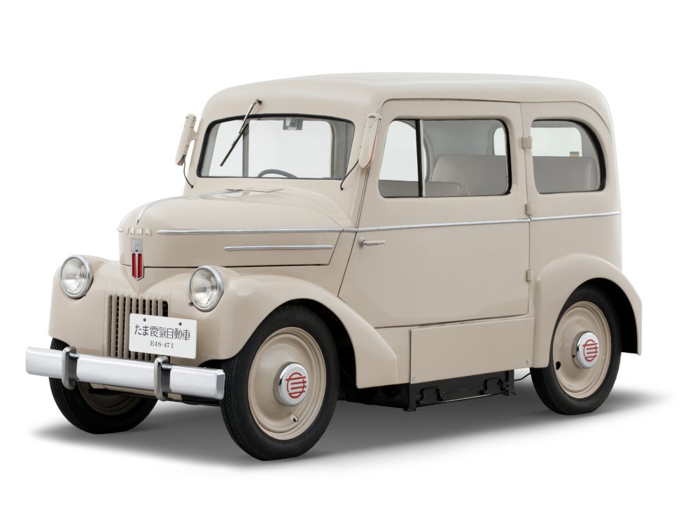 Photo couleur d’une camionnette légère de style années 1940 avec une plaque d'immatriculation japonaise et un ornement de capot indiquant « TAMA ».