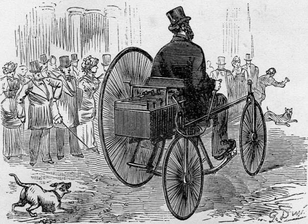 Gravure sur bois d'une foule stupéfiée regardant un homme en manteau et à chapeau haut de forme conduire un véhicule électrique à trois roues dans une rue pavée, poursuivi par plusieurs chiens qui aboient.