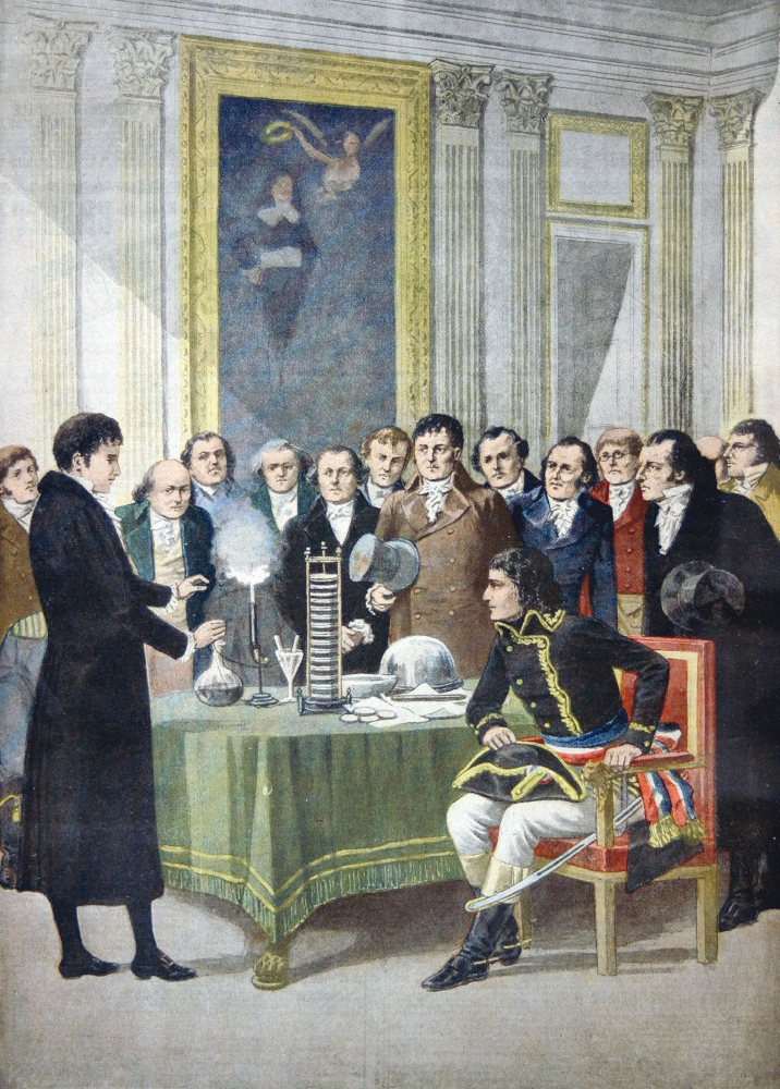 Gravure colorée sur bois d'un homme qui fait une démonstration d'un appareil électrique produisant des étincelles à un groupe d'hommes en tenue formelle du 19e siècle, parmi lesquels est assis Napoléon Bonaparte.
